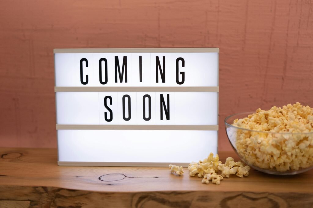 Lightbox sign displaying 'Coming Soon' next to a bowl of popcorn on wooden surface.